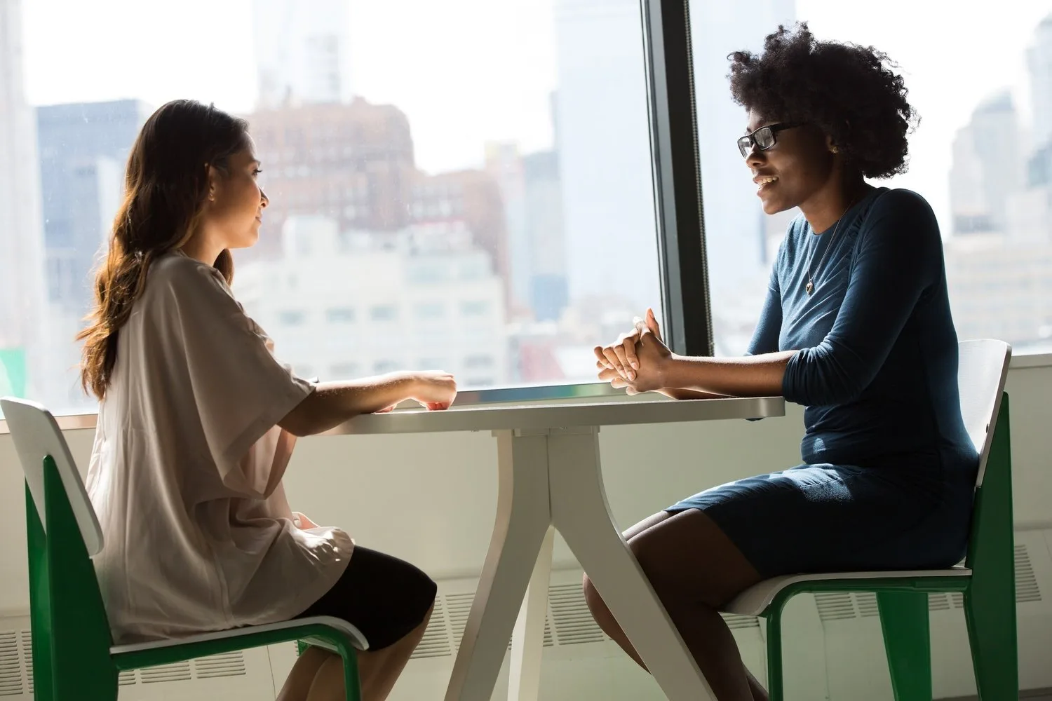 Two women talking across a small round table in a sunny room