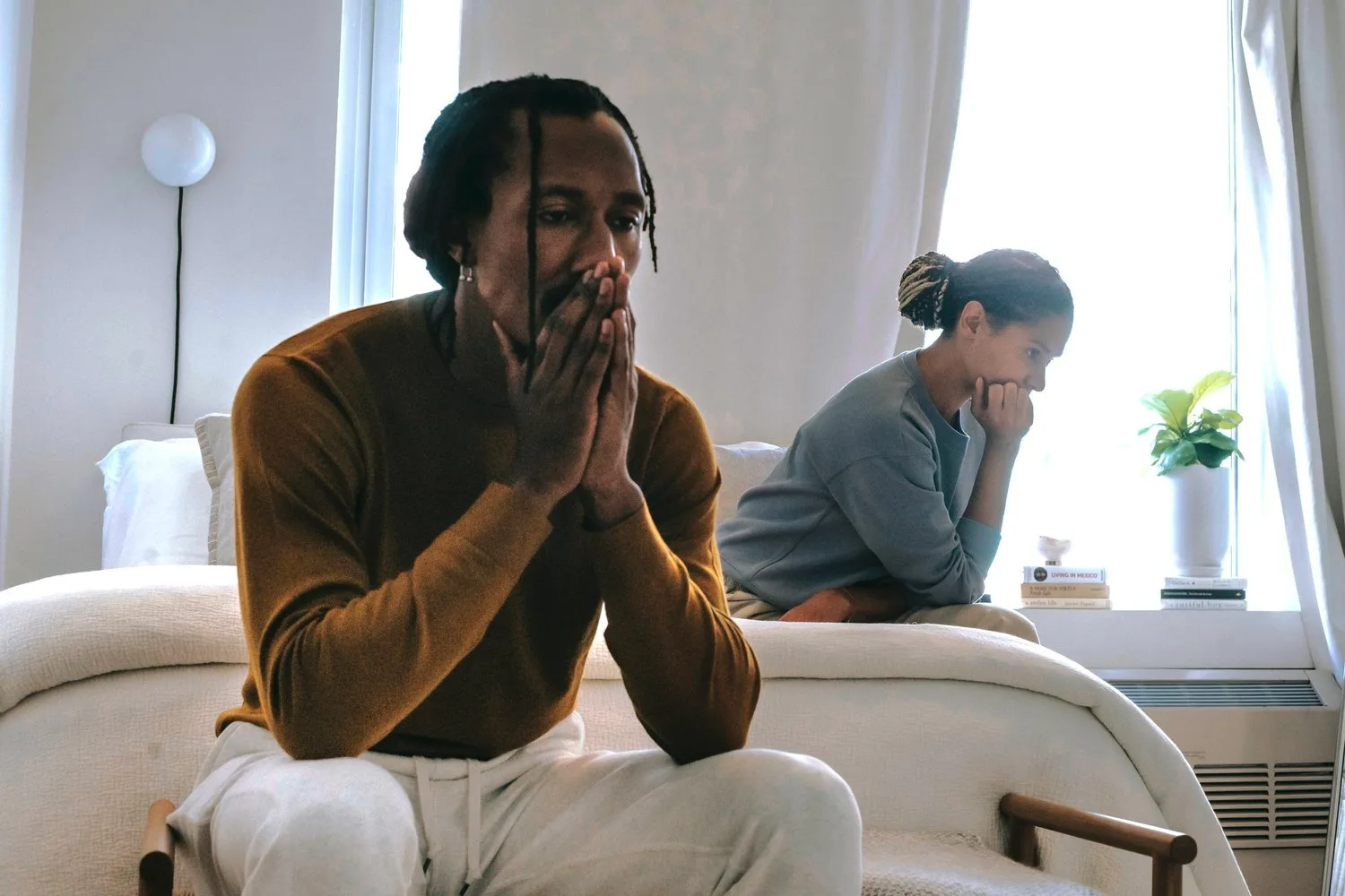 Man with hands pressed together near his face talking with a therapist in a bright room