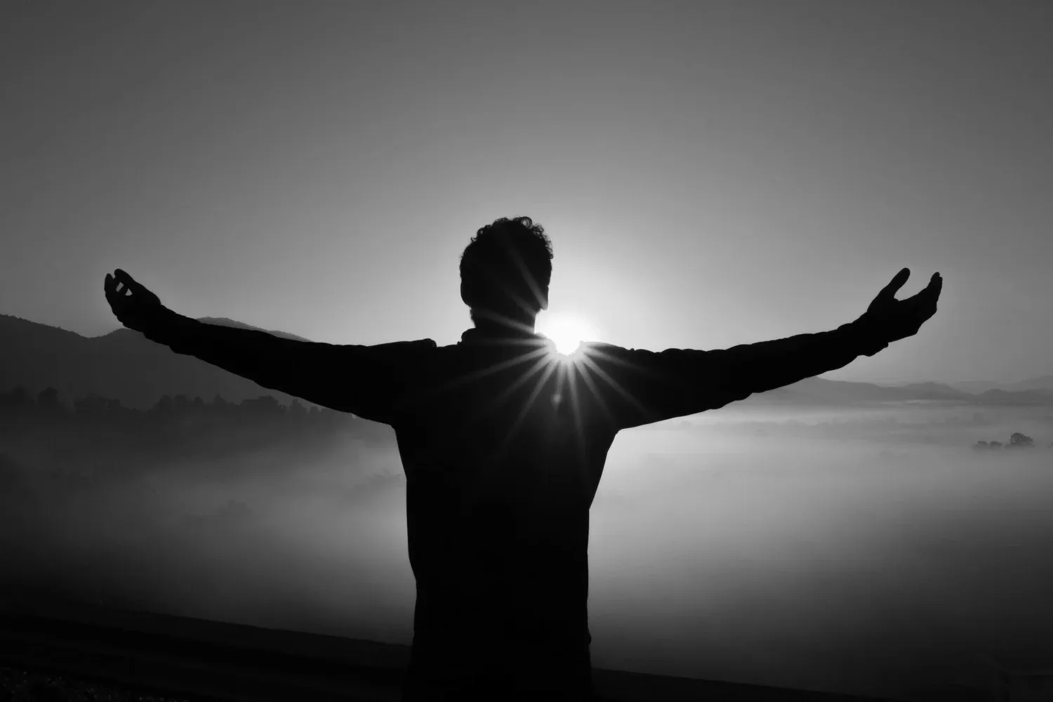 Silhouette of a person with arms outstretched against the sun