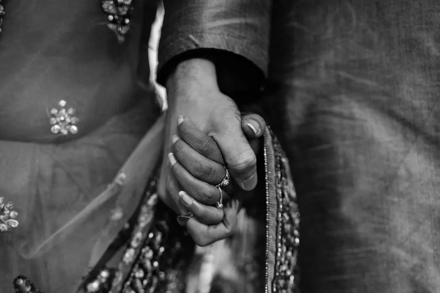 Black-and-white close-up of two people in traditional dress holding hands