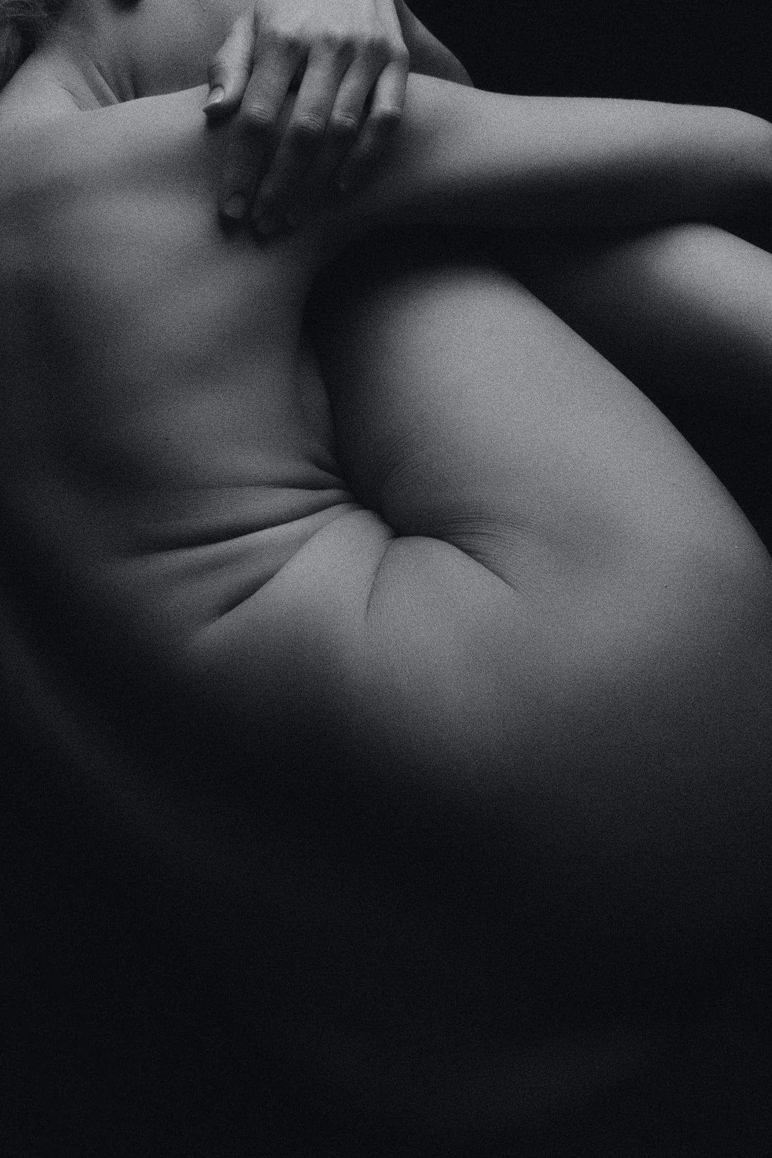Black-and-white close-up of a person’s arms wrapped around their knees