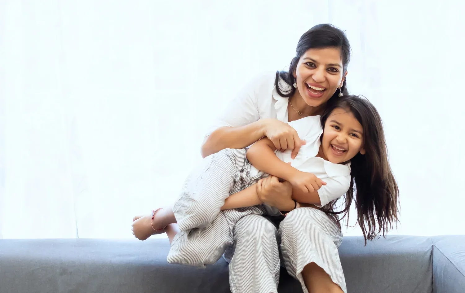 Smiling mother and daughter hugging on a sofa