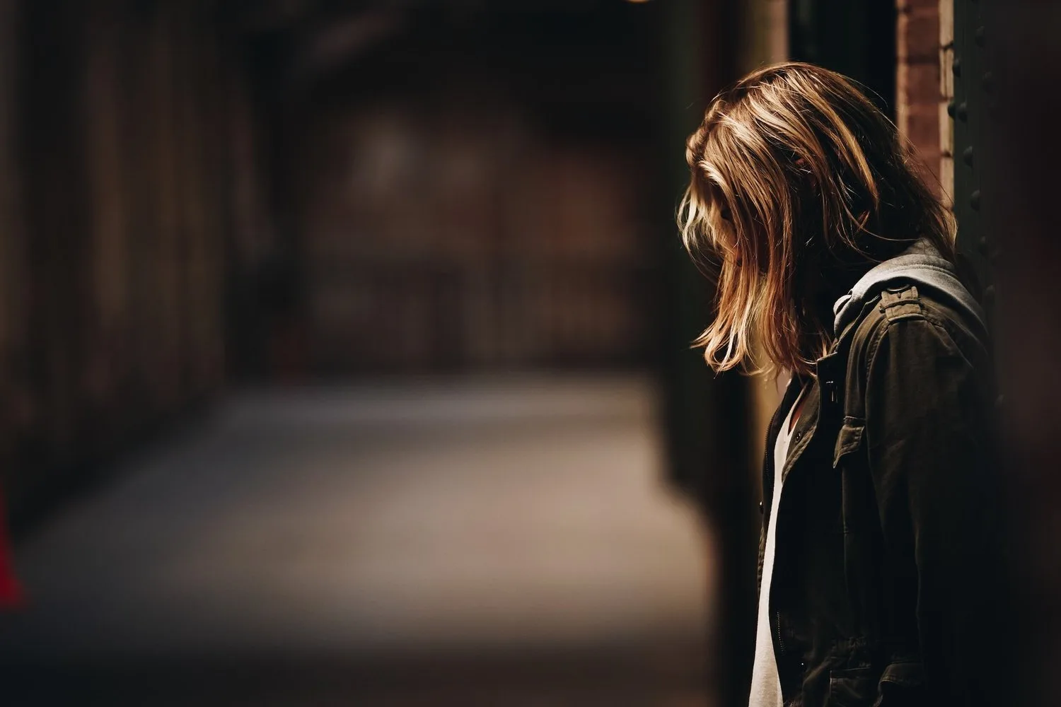 Person with long hair standing in a dim, shadowy room