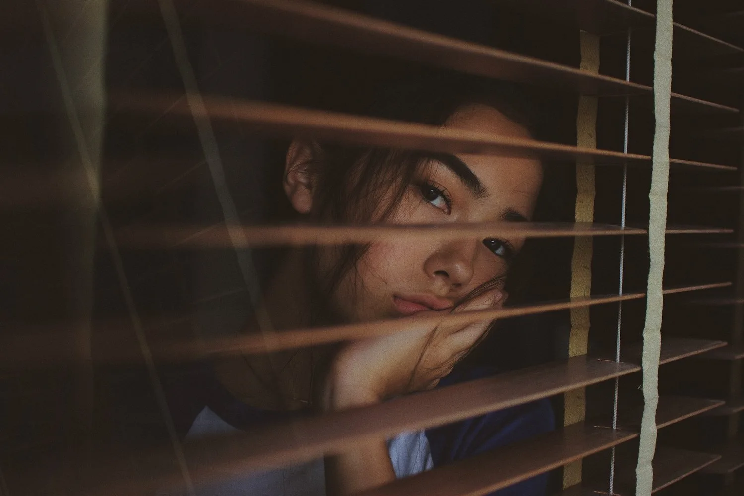 Person peering through the slats of window blinds