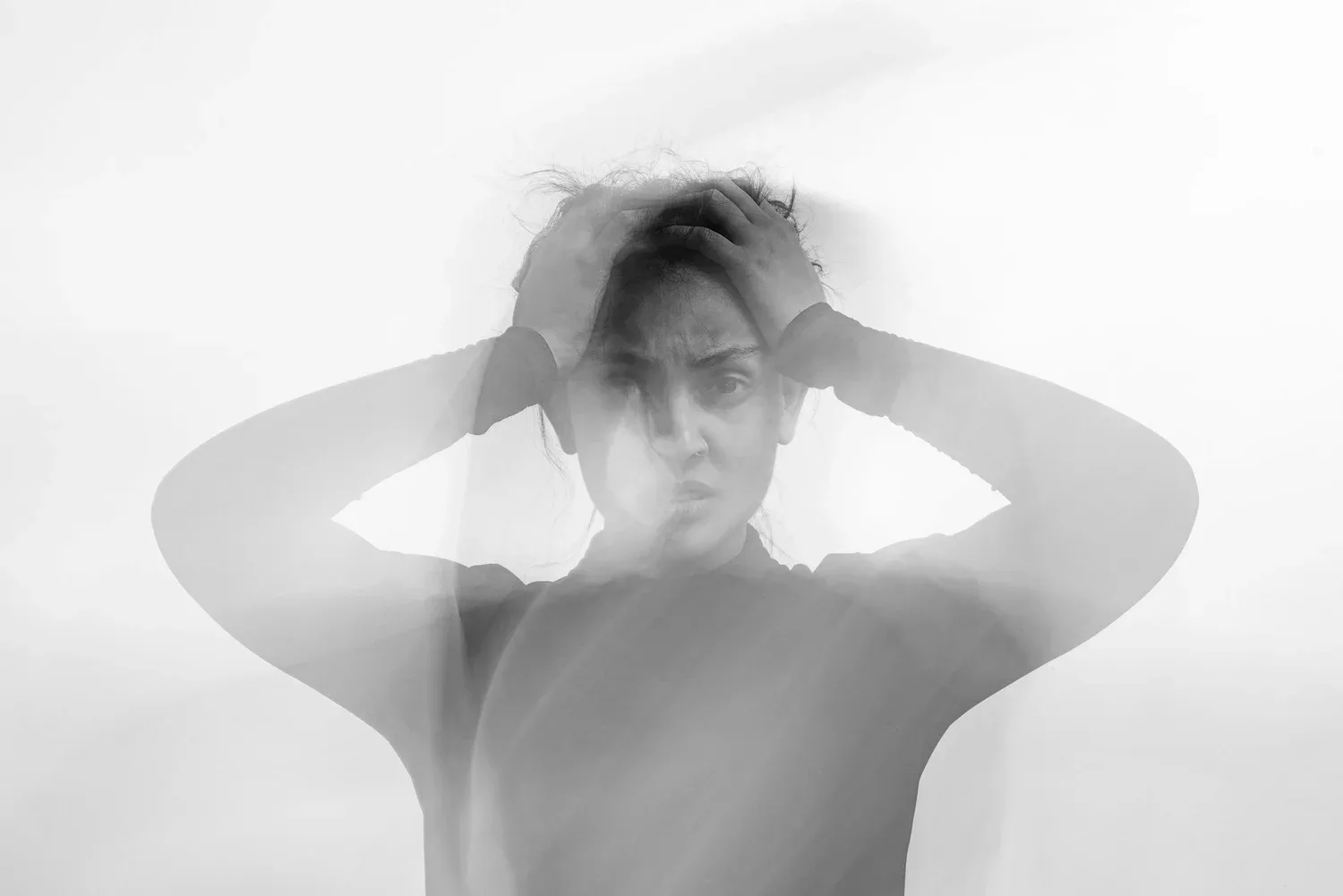 Black-and-white photo of a person with hands in their hair, eyes closed