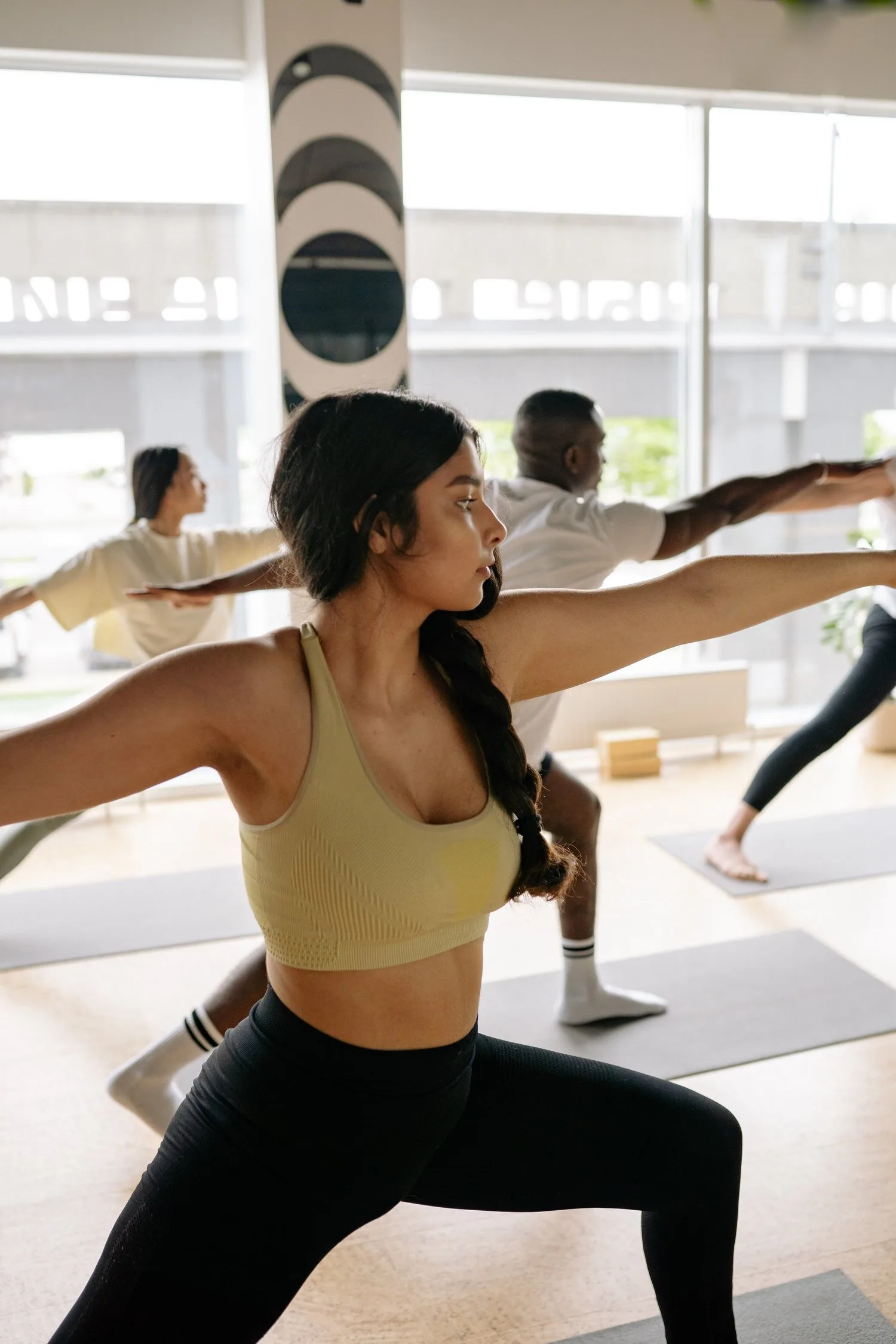Woman in a warrior stretch during a group movement class in a bright studio