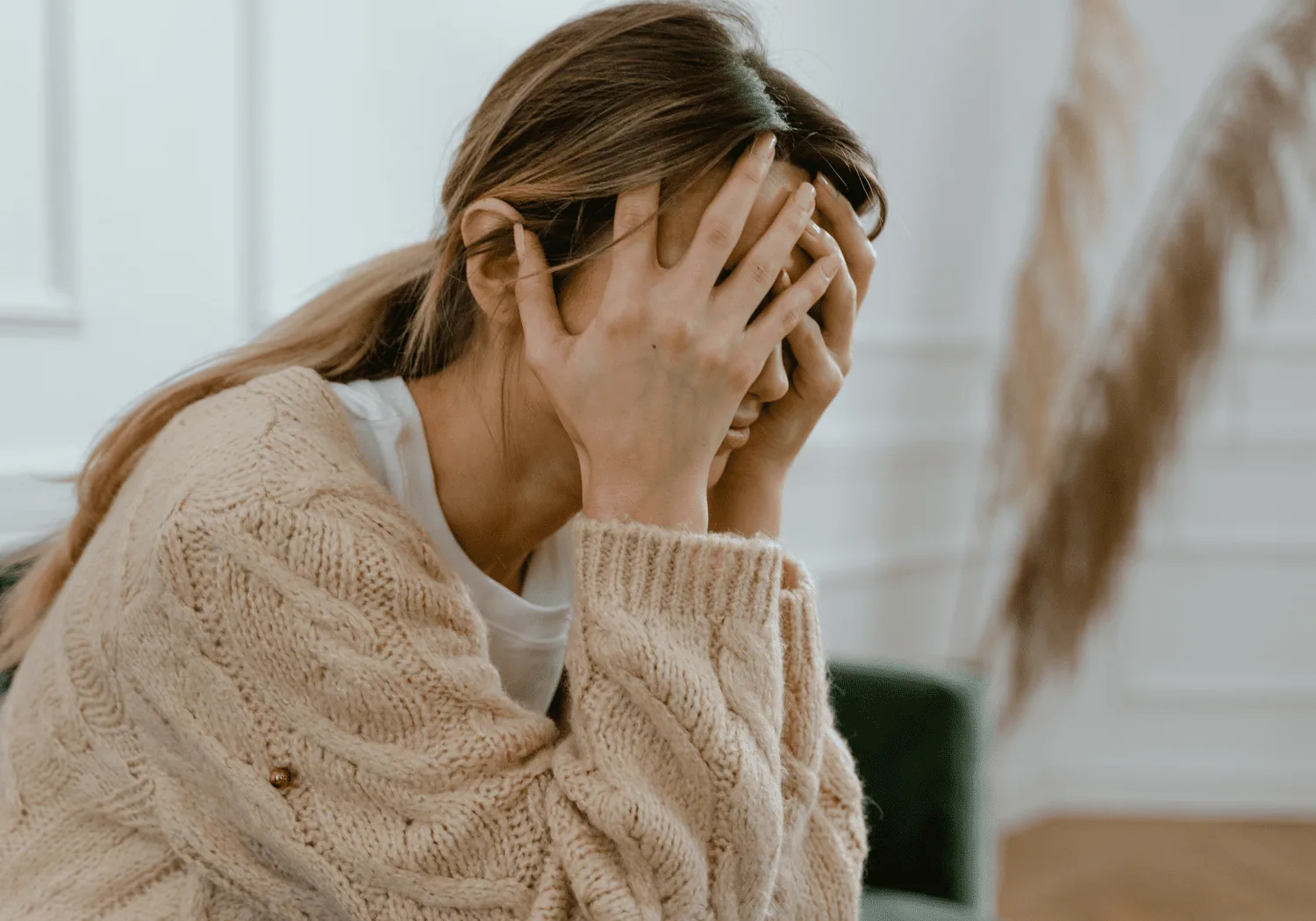 Woman in a cream sweater covering her face with both hands