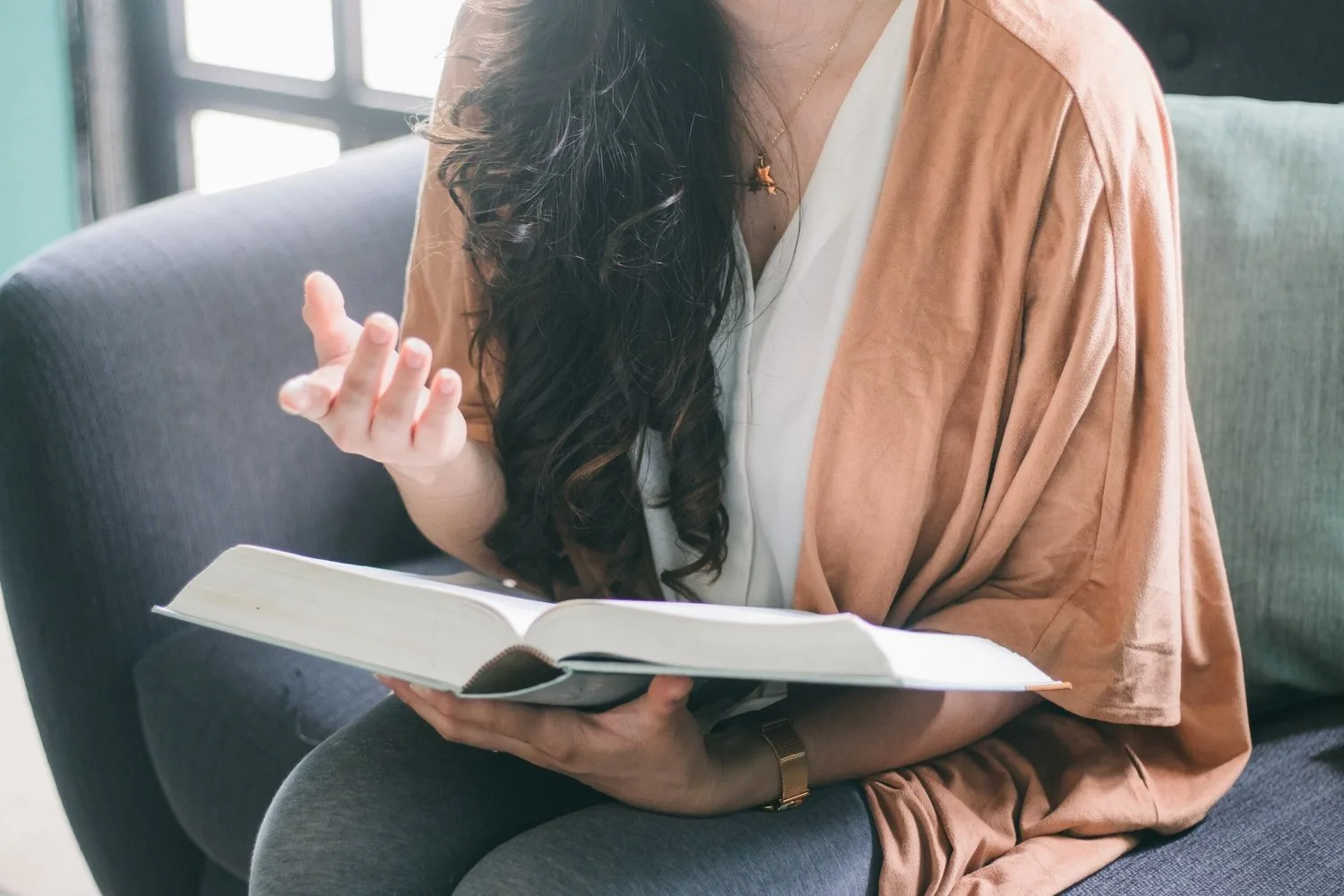 Woman reading a book on a sofa, wrapped in a cardigan