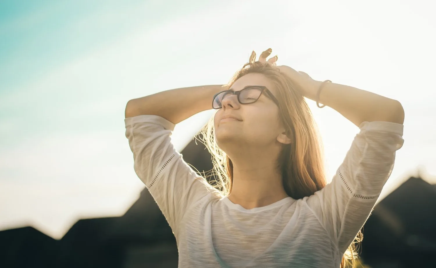 Woman with hands on her head and eyes closed, face lifted toward the sun