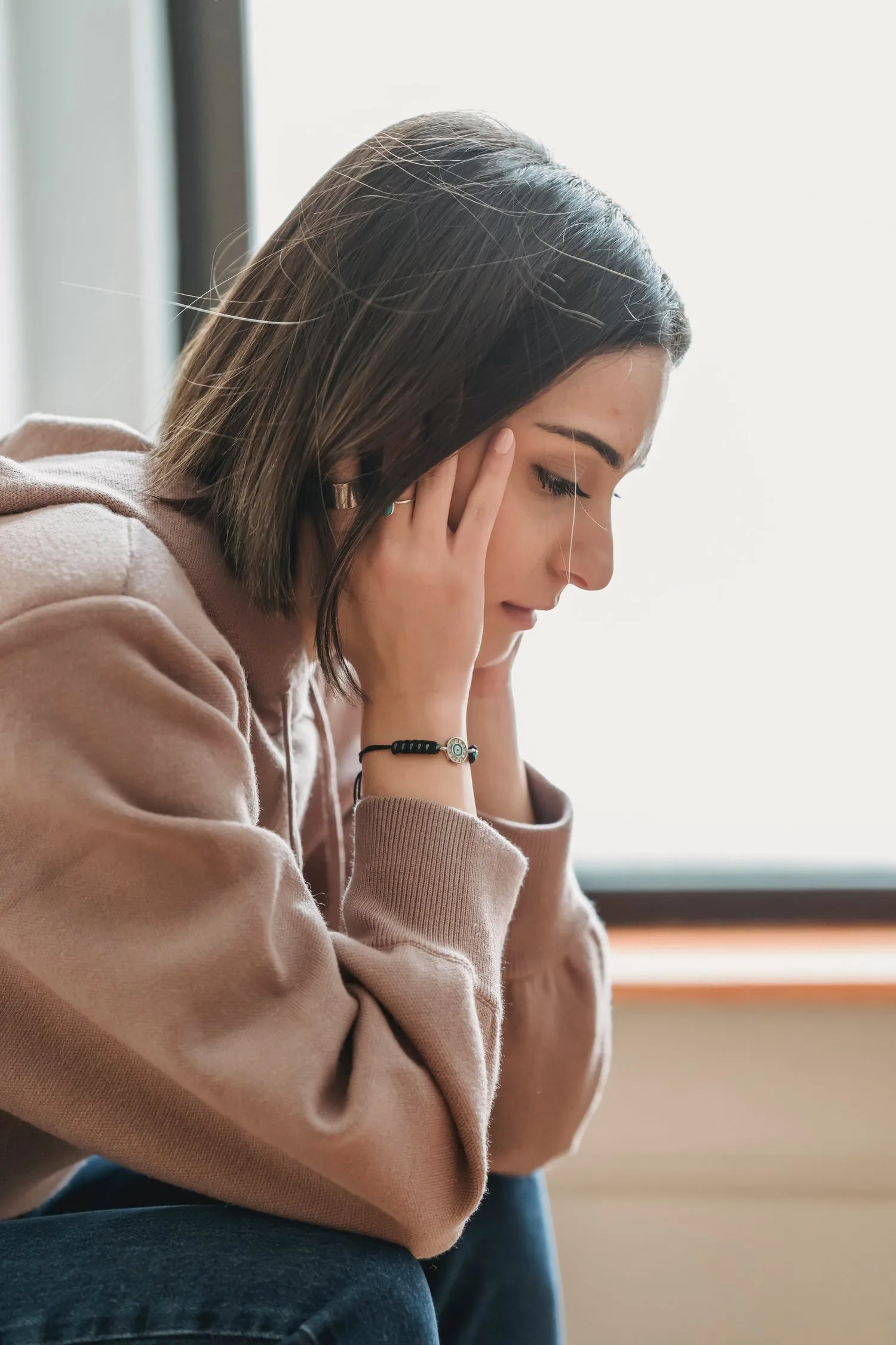Young woman with a hand to her head, looking down in thought