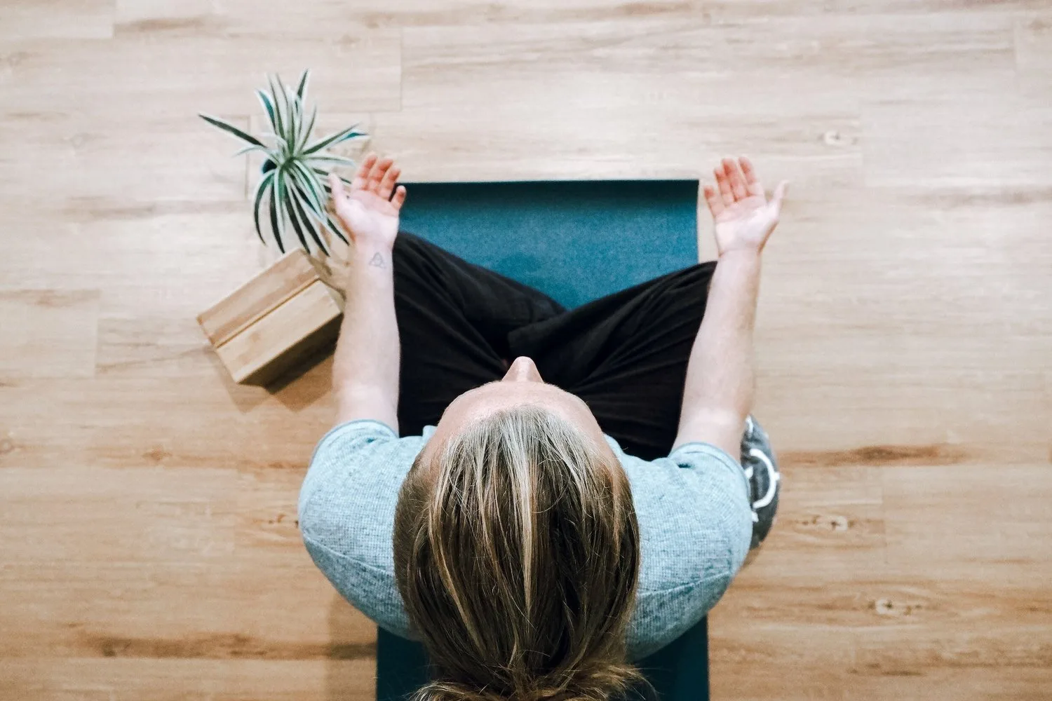 Person meditating cross-legged on a wooden floor, seen from above
