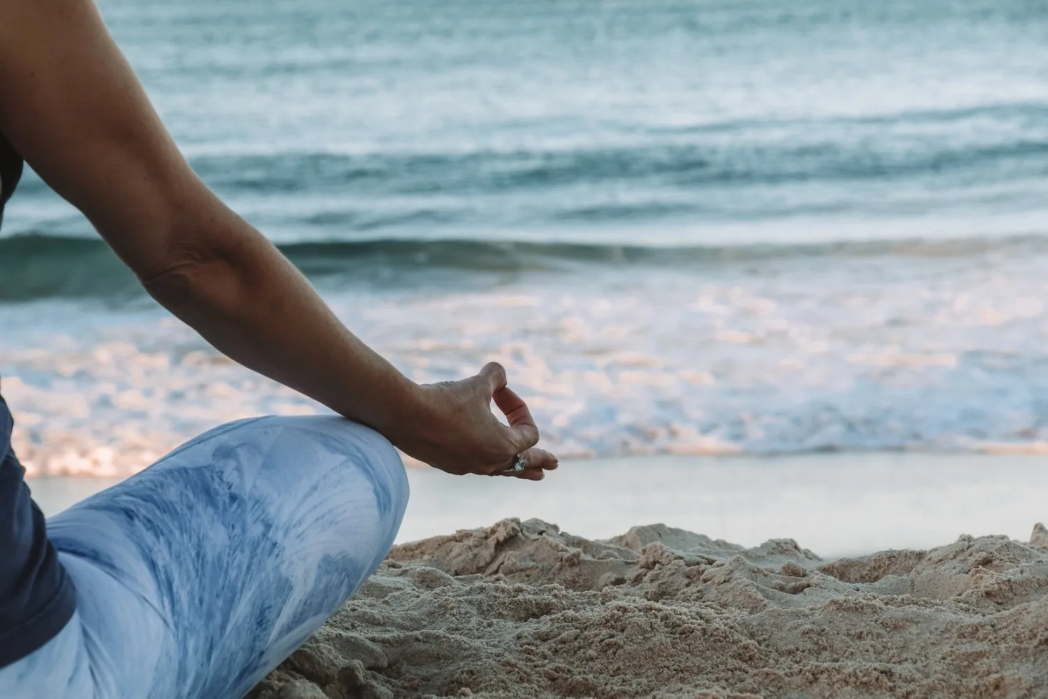Person meditating on a sandy beach as waves roll in