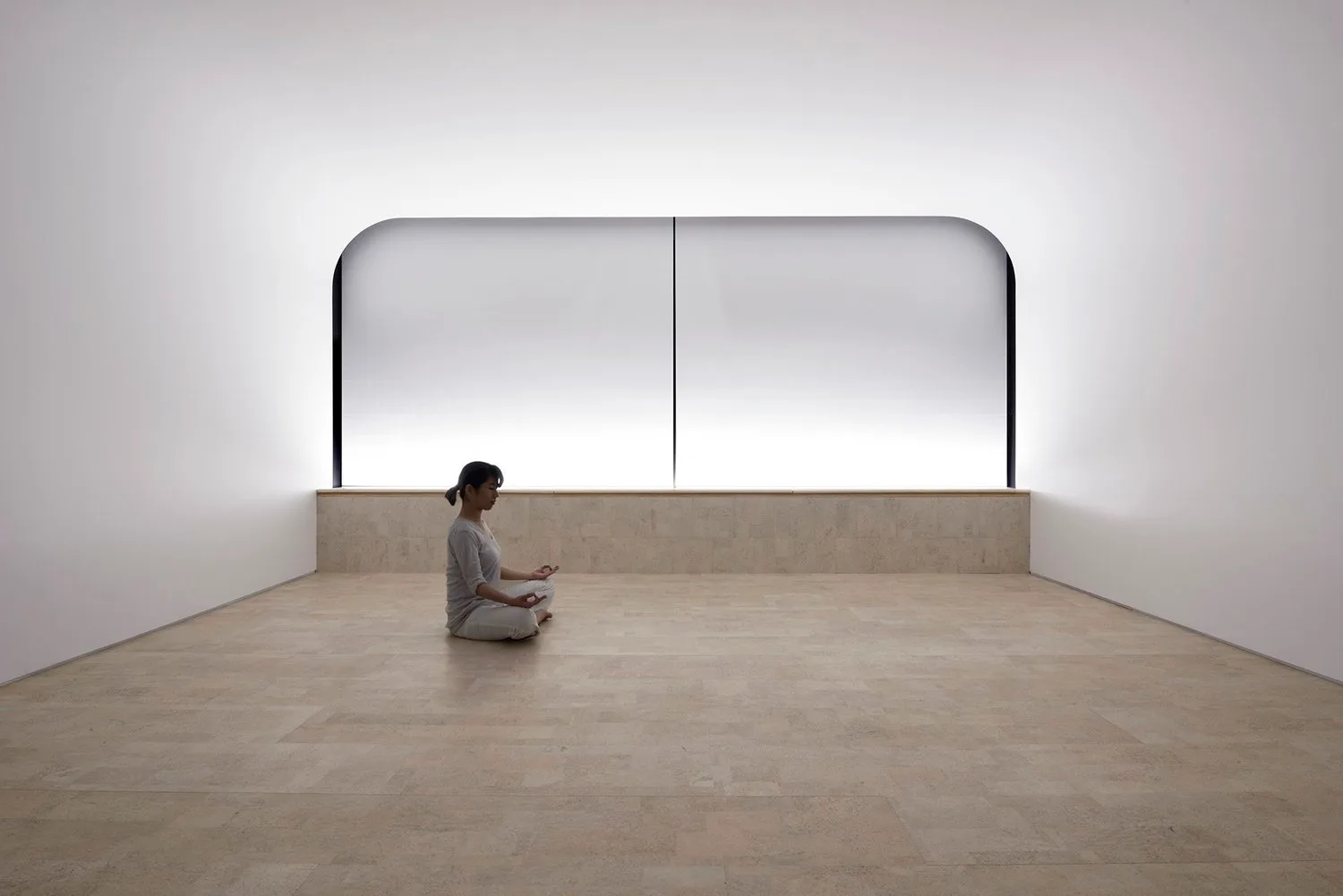 Single person sitting alone in a large, empty, softly lit room