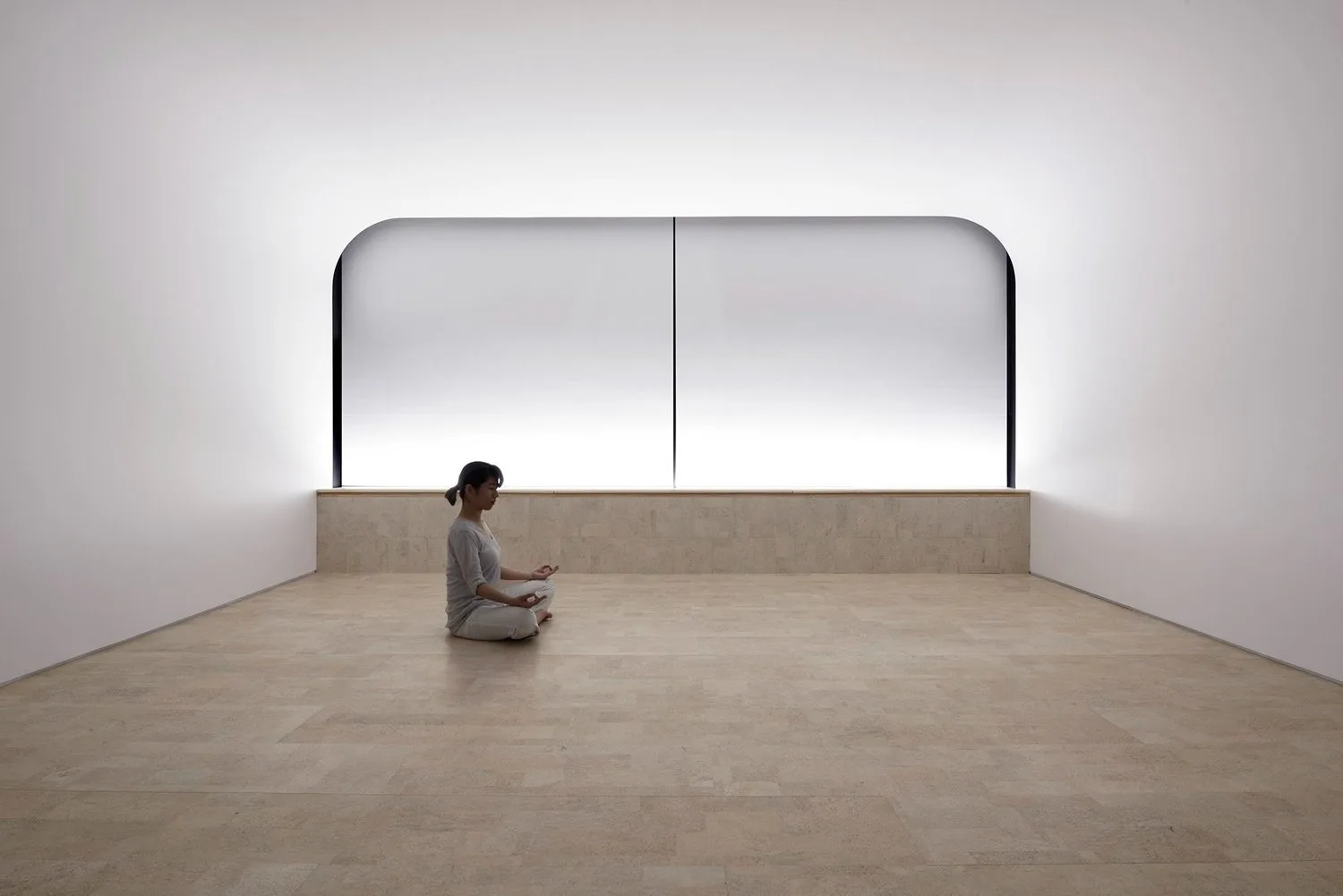 Single person sitting alone in a large, empty, softly lit room