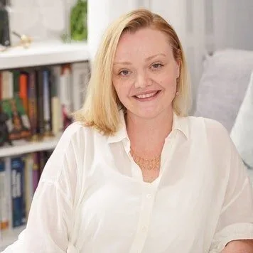 Portrait of a smiling woman with blonde hair in a white shirt in front of bookshelves