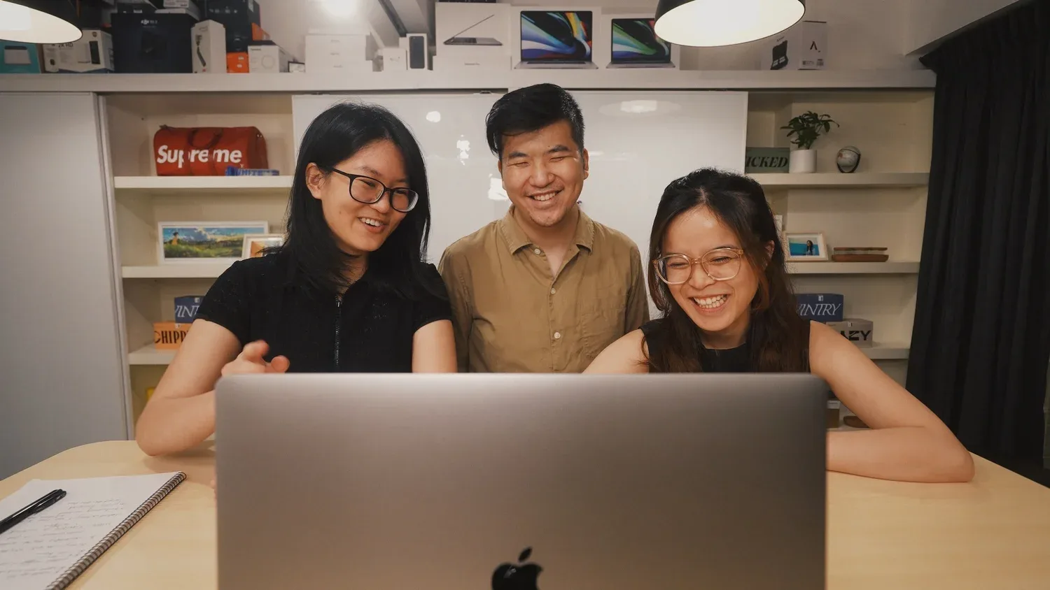 Three smiling young adults gathered around a laptop