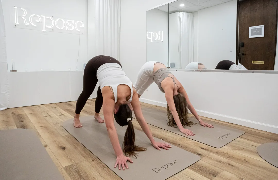 Two women in a downward-facing stretch on mats in the Repose studio