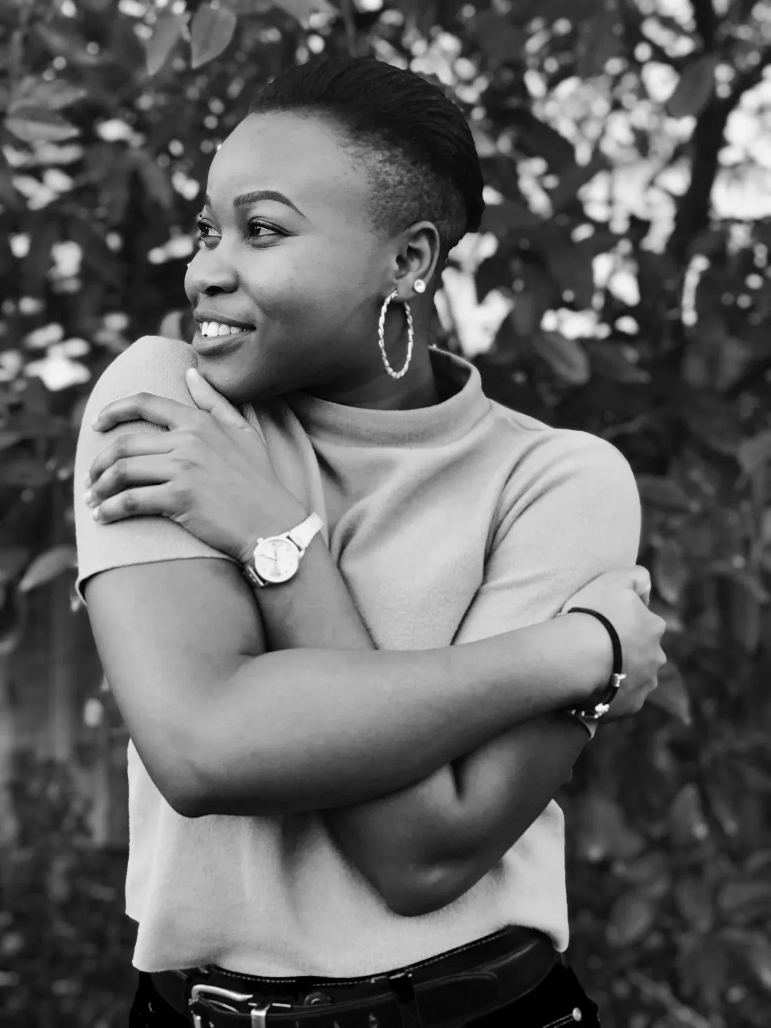 Black-and-white photo of a smiling woman hugging herself outdoors