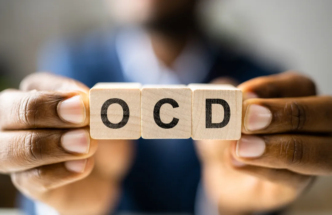 Hands holding wooden letter tiles that spell OCD