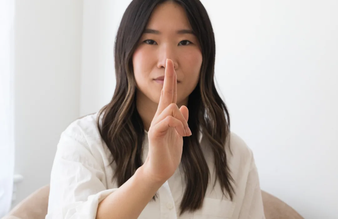 Woman in white holding a finger to her lips in a quiet gesture