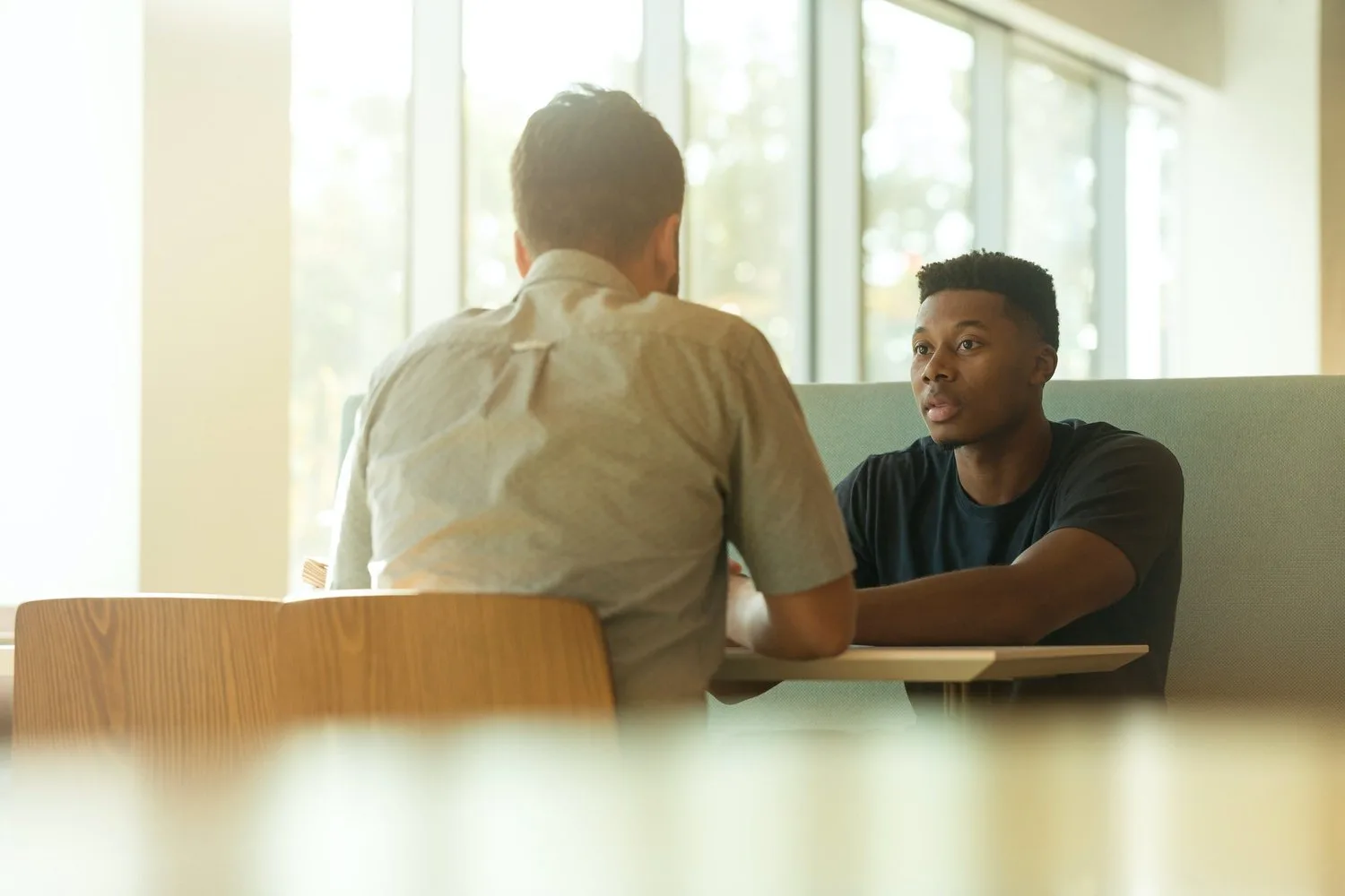 Two men talking across a table in a sunlit room