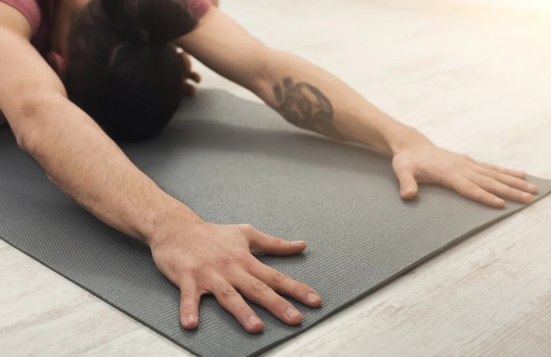 Person in a forward stretch with hands resting on a gray mat