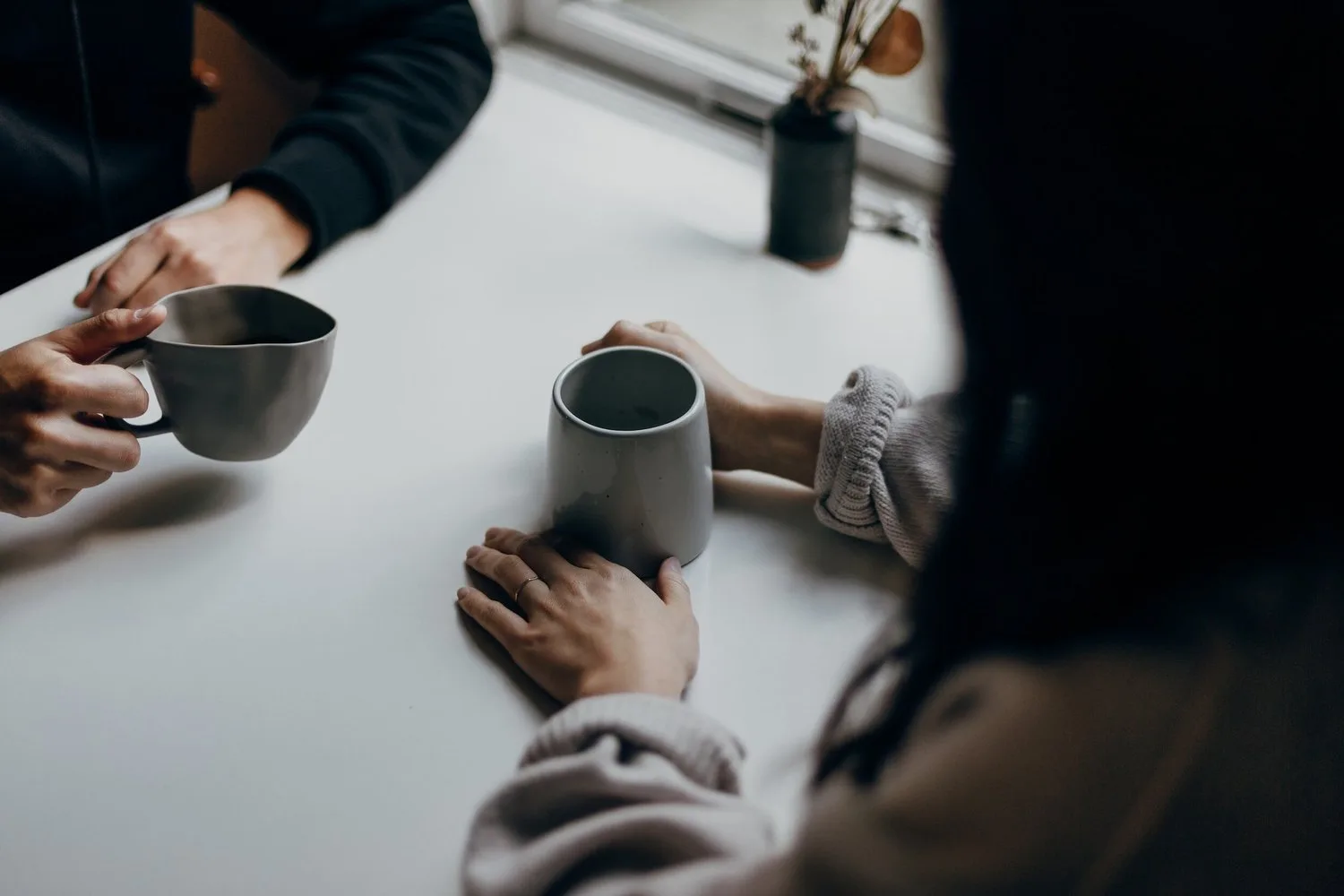 Two people seated at a table with mugs, one holding a small book