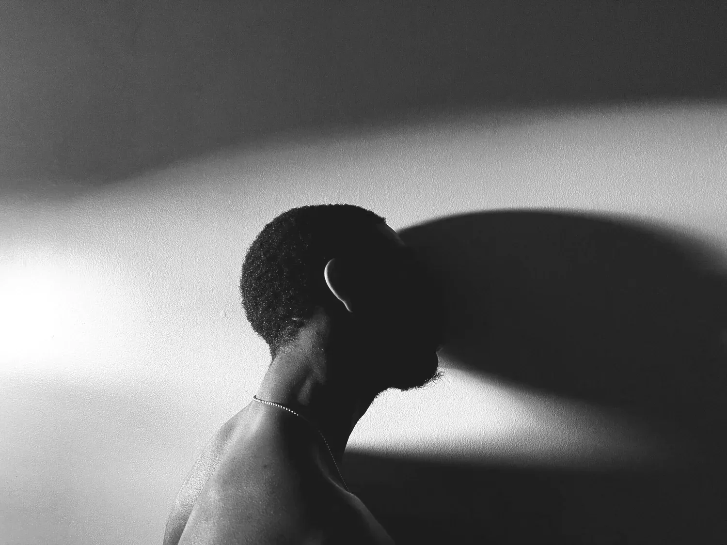 Black-and-white photo of a person resting their head against a wall in soft light