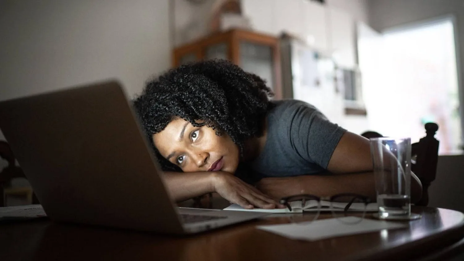 Exhausted woman resting her head on her arms beside an open laptop