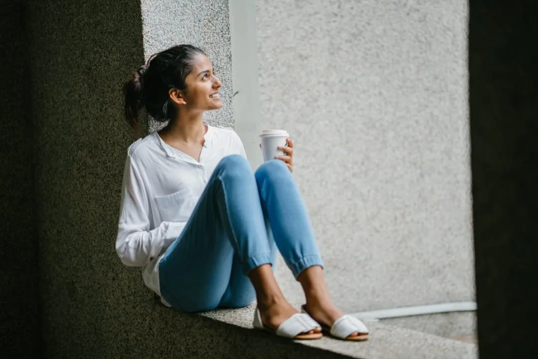 Woman sitting on a window ledge holding a mug, gazing outside