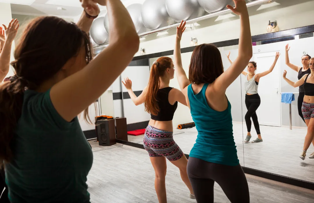 Group of women dancing with arms raised in a mirrored dance studio