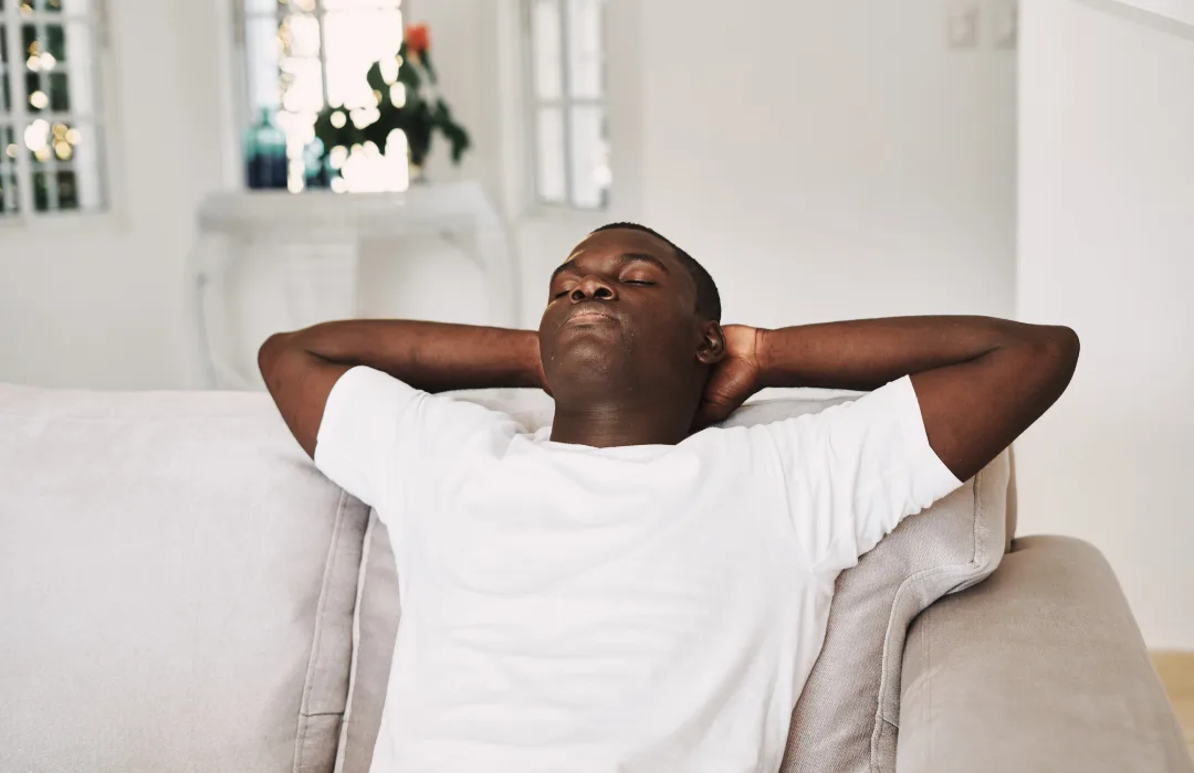 Man leaning back on a sofa with hands behind his head, eyes closed and relaxed