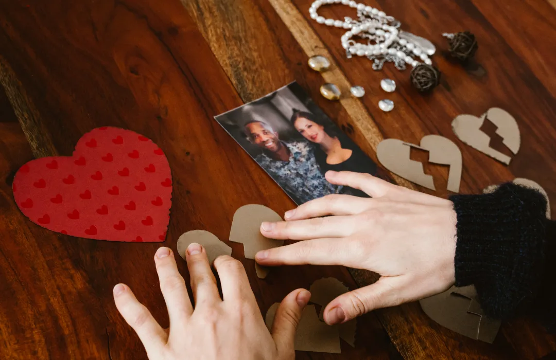 Hands arranging paper hearts, photos, and keepsakes on a wooden table