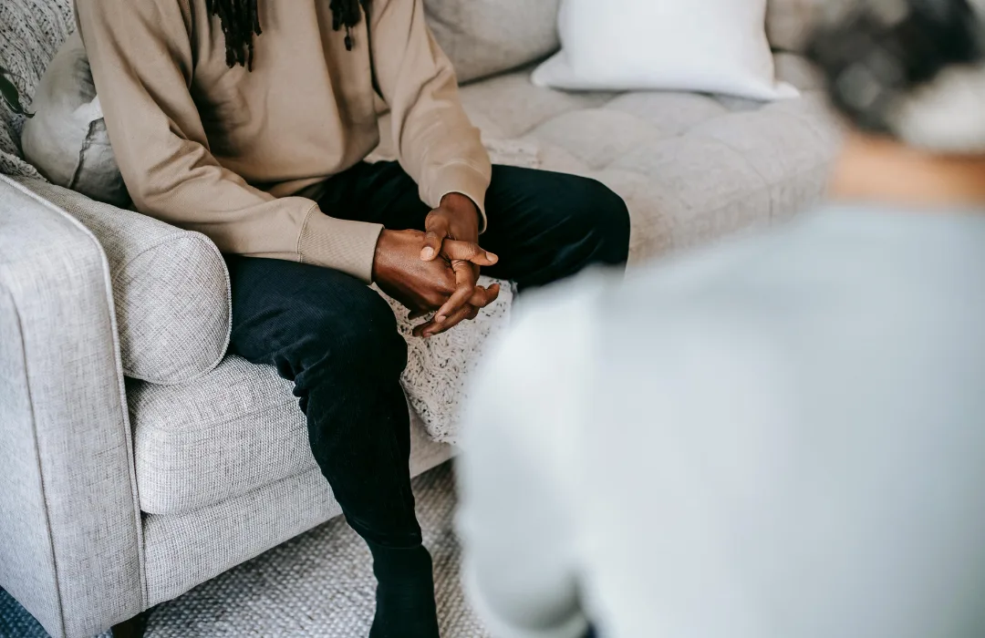 Two people seated on a sofa with hands clasped, one leaning in to listen