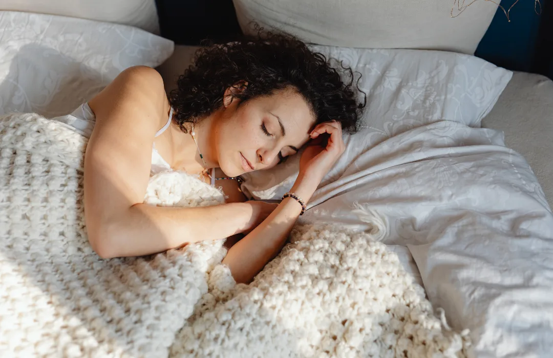 Woman resting in bed on a knit blanket with a hand under her cheek