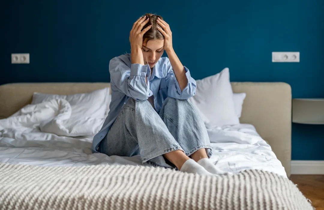 Stressed woman sitting on a bed holding her head in both hands