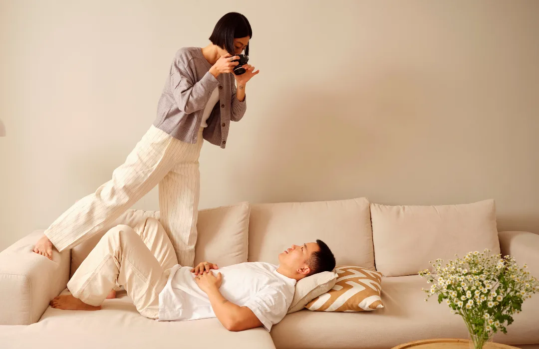 Person taking a photo of a woman lying on a sofa, as for social media