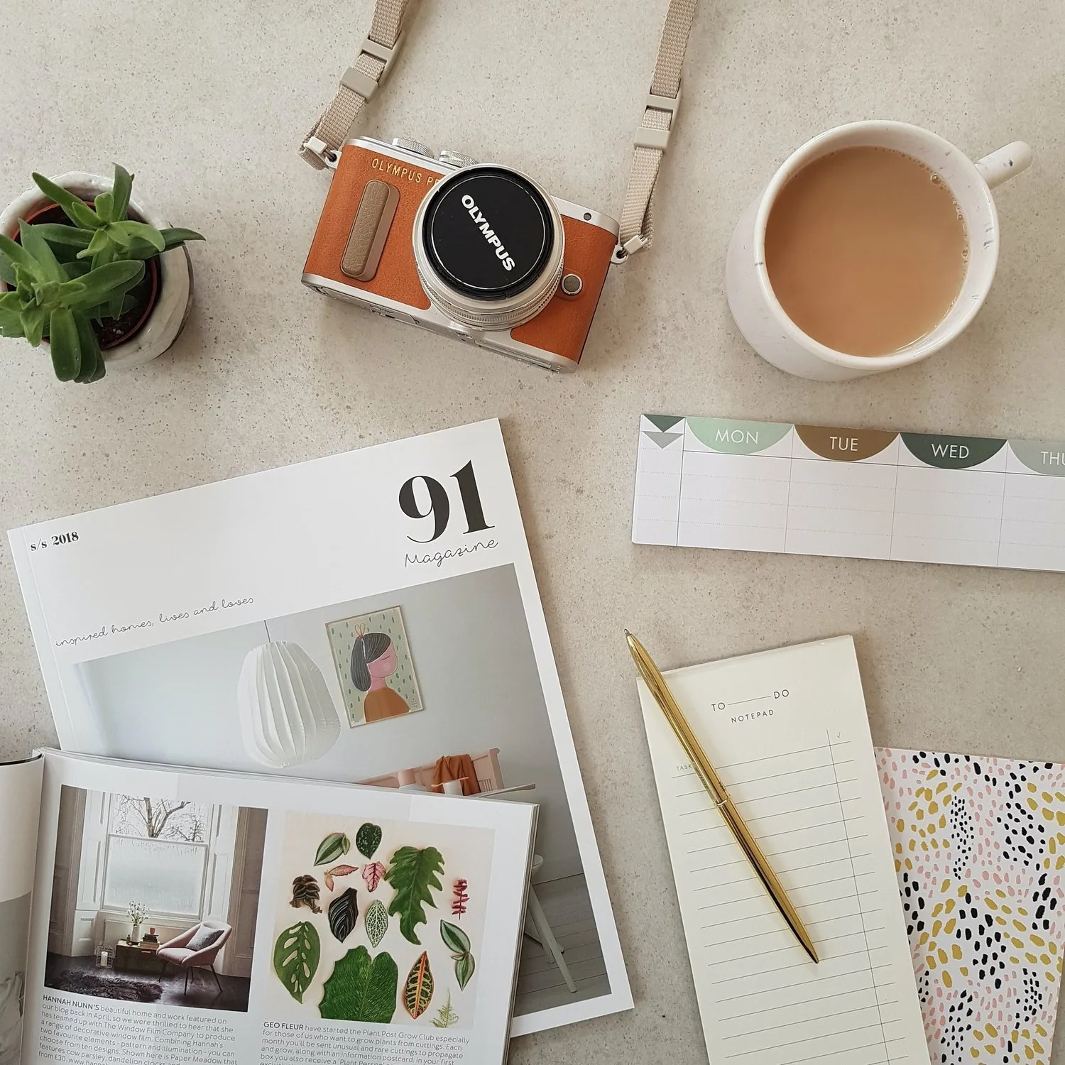 Flat lay of a camera, coffee, magazine, and notebook on a desk