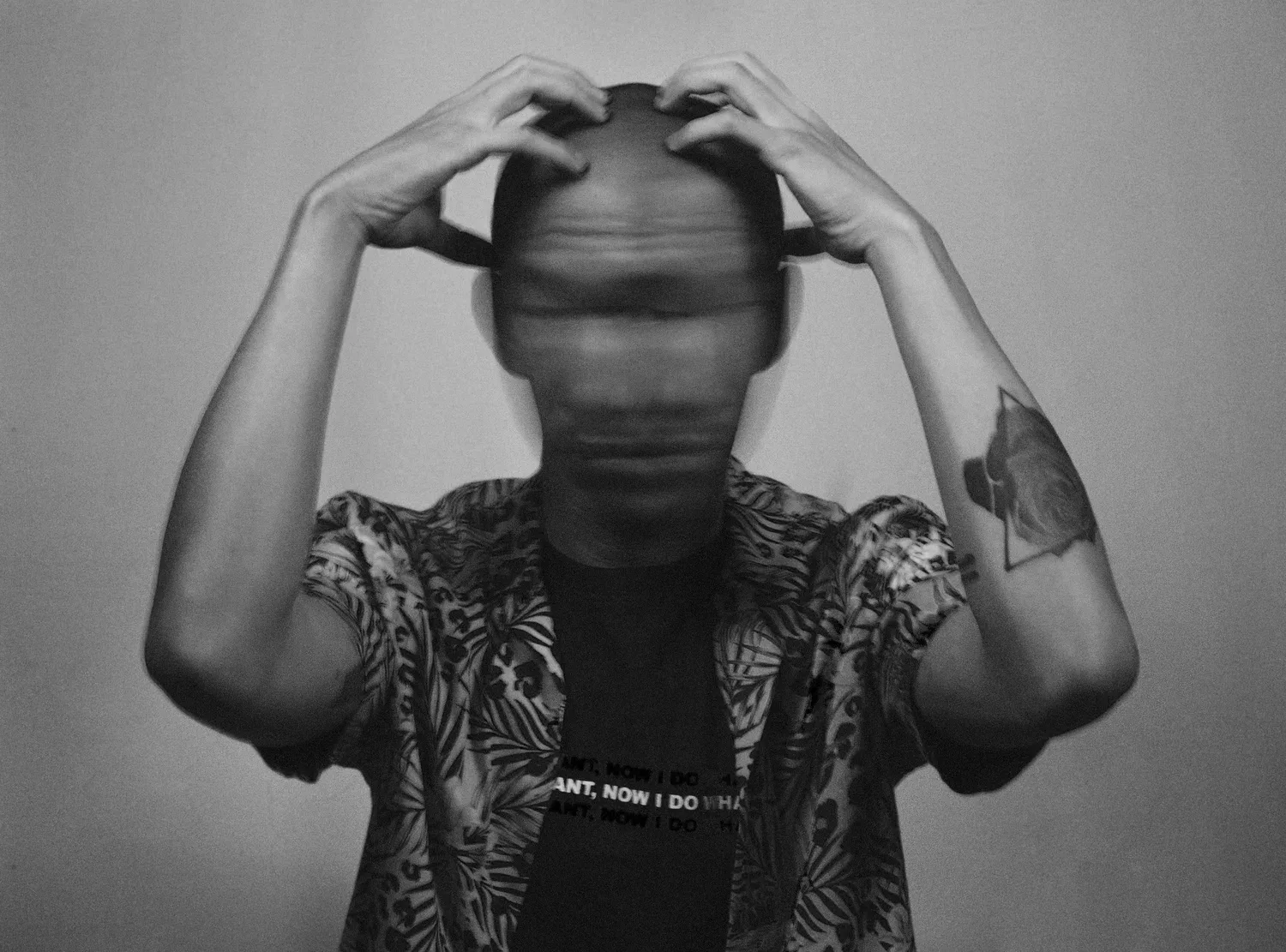 Black-and-white photo of a person with hands on their head, face blurred