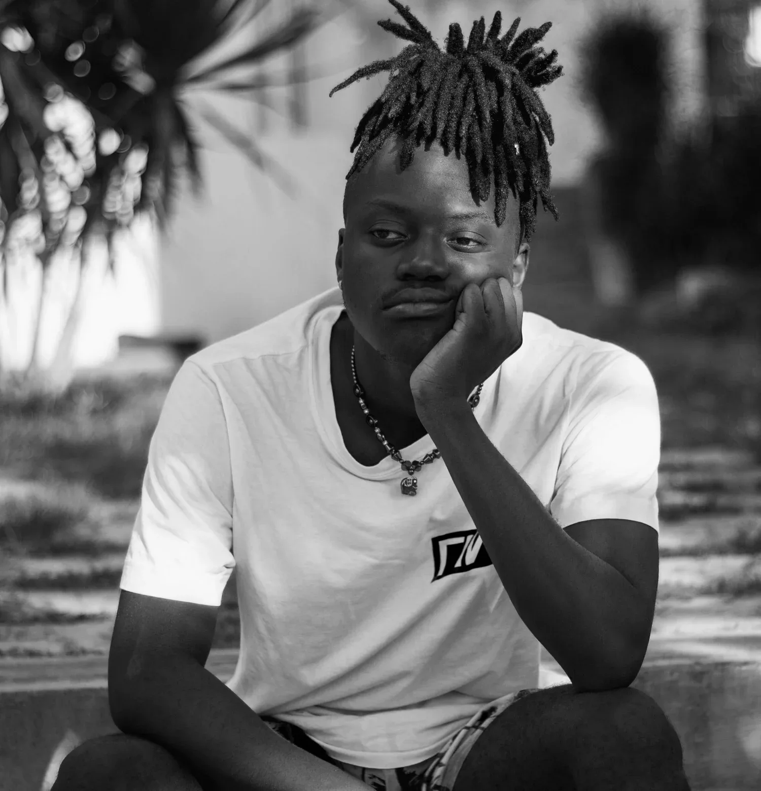 Black-and-white photo of a young man with locs resting his chin on his hand