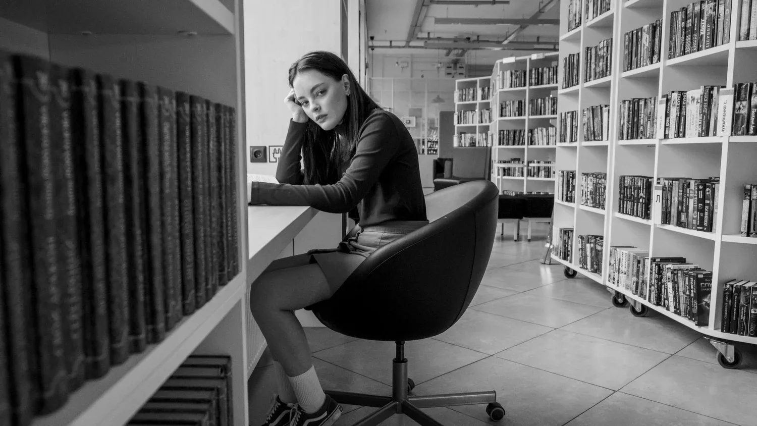 Woman sitting at a desk between tall bookshelves in a library