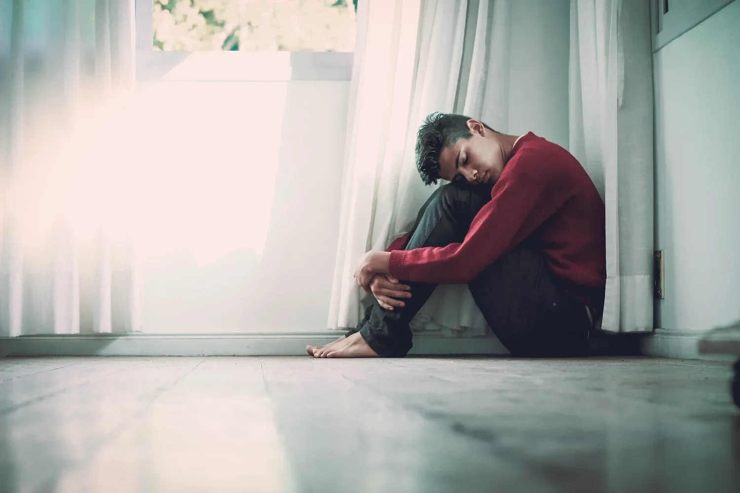 Person sitting on the floor hugging their knees in a softly lit room