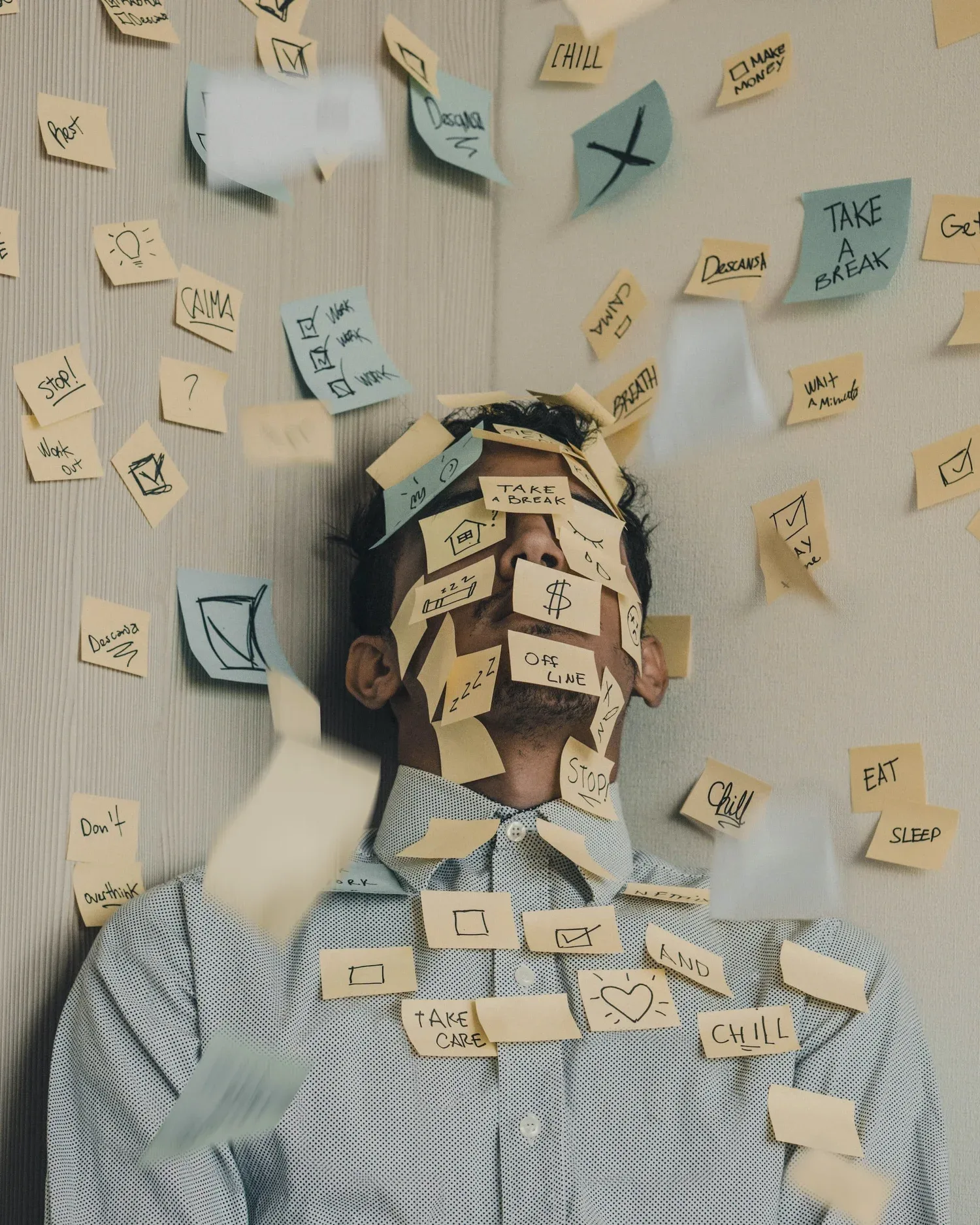 Person whose face is covered in sticky notes against a wall of notes