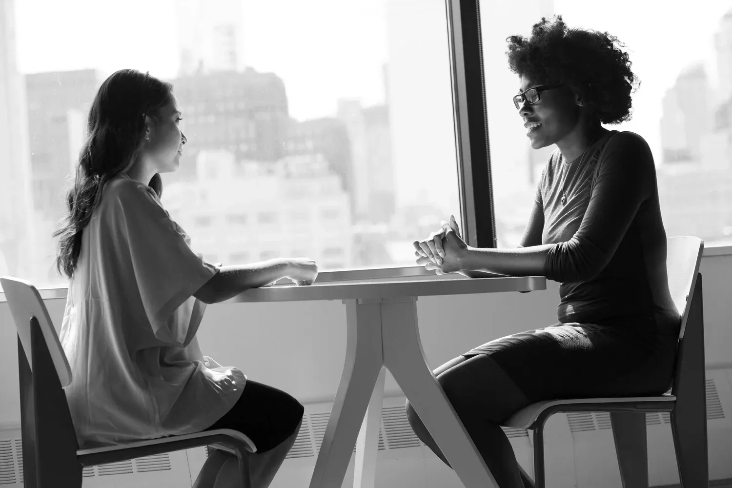 Black-and-white photo of two women talking across a small round table