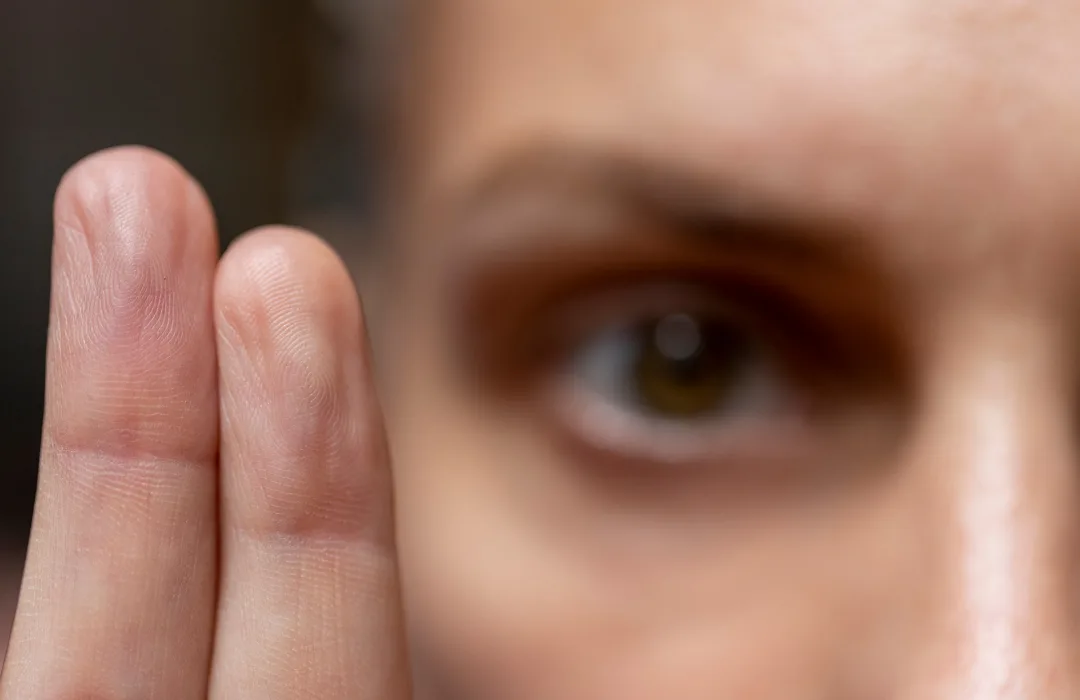 Close-up of a person’s eye peering between two fingers