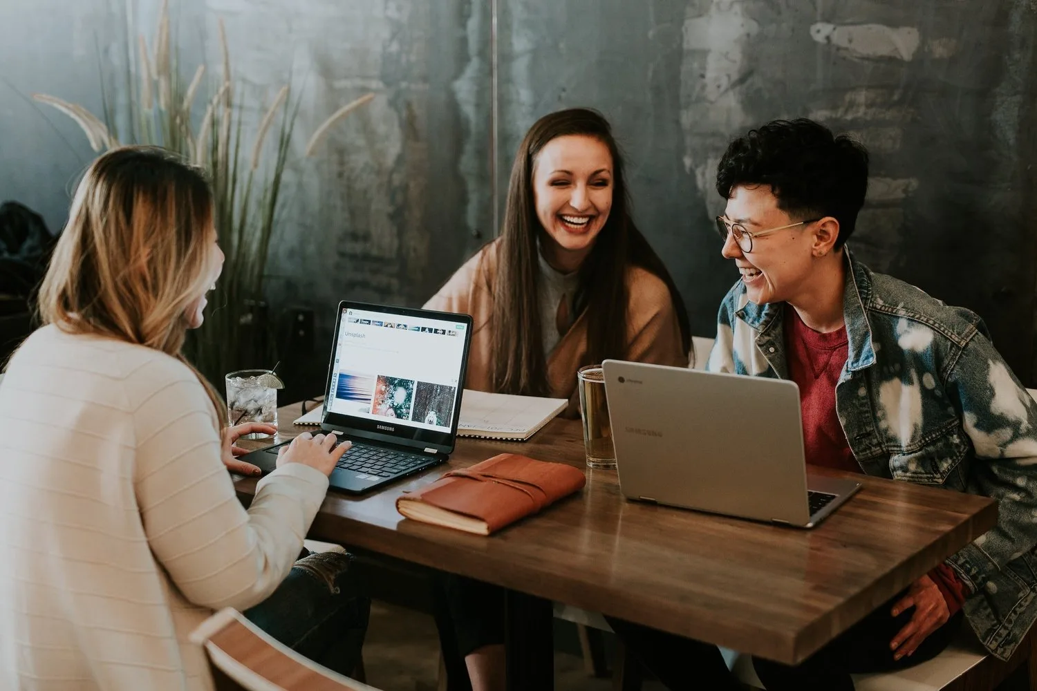 Three young women laughing together at a café table with laptops