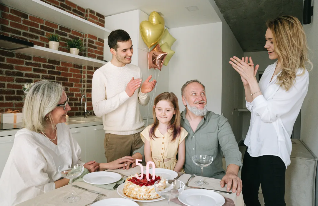 Family celebrating a birthday around a table with a cake and balloons