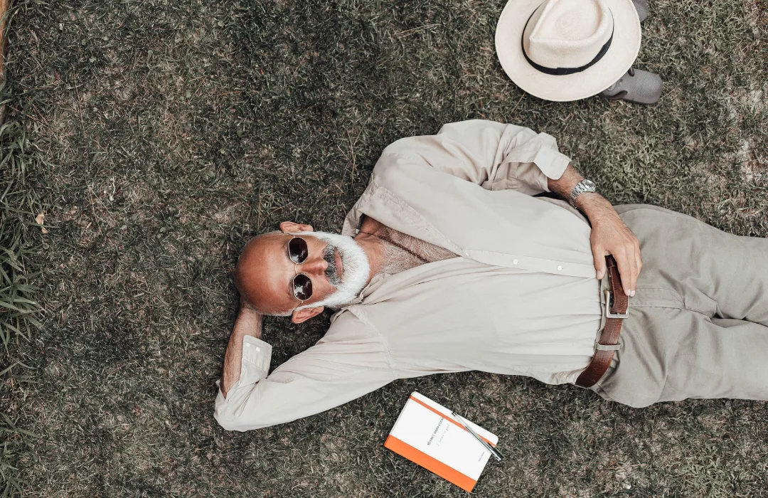 Smiling older man lying on a textured rug beside a hat and a small box