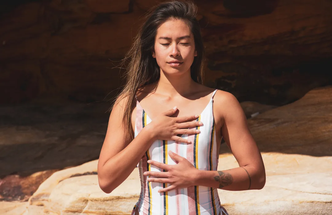 Woman with eyes closed placing one hand on her chest and one on her belly