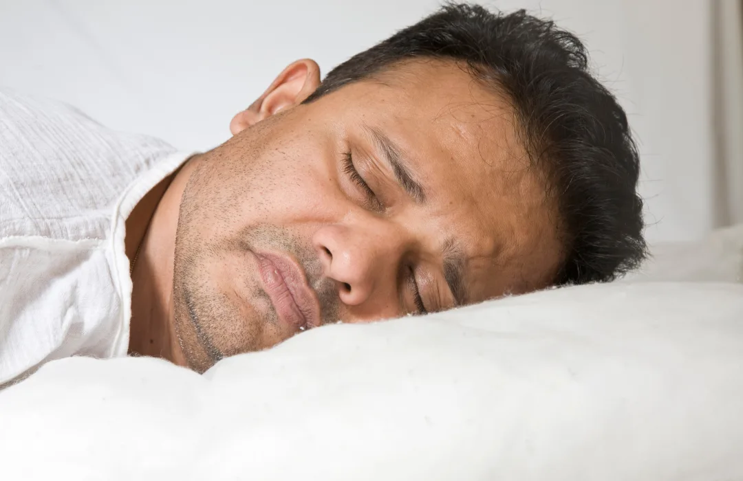 Man sleeping with his face on a white pillow